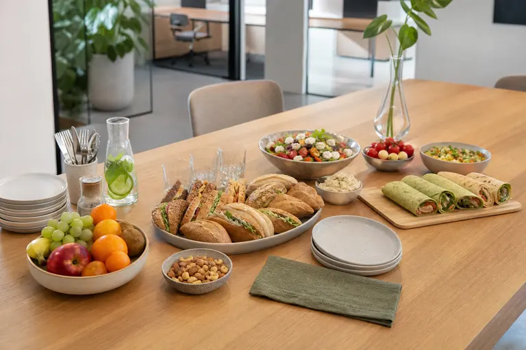 Bedrijfslunch met broodjes, wraps, salades en fruit op een kantoortafel